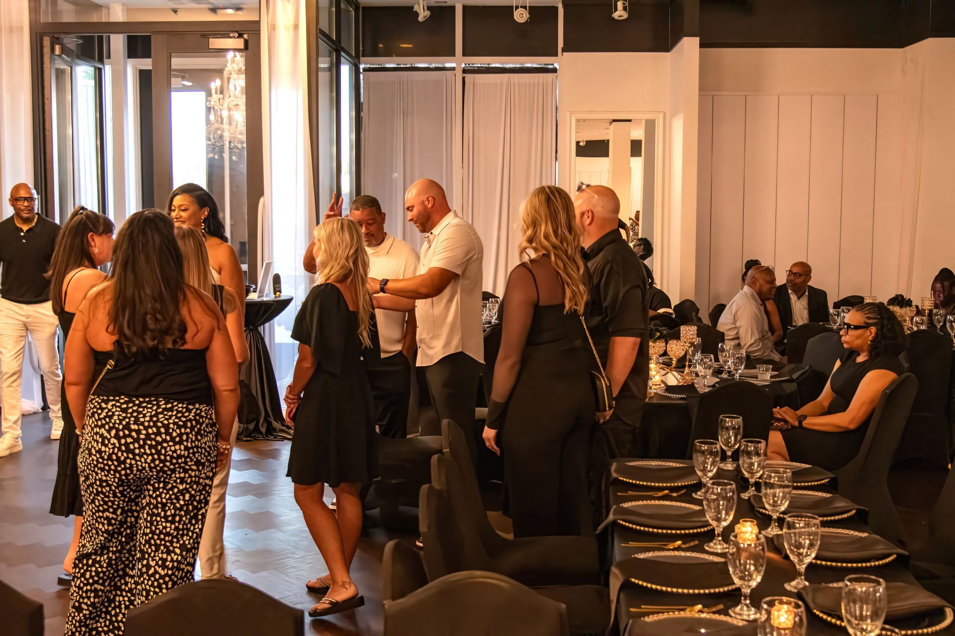 A group of people gathers in a well-lit, elegantly decorated indoor space, with some socializing near a dining table.