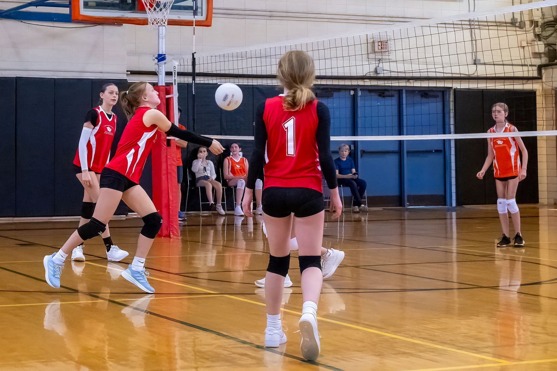 A volleyball team in red jerseys plays a match on an indoor court, with one player mid-bump to return the ball.