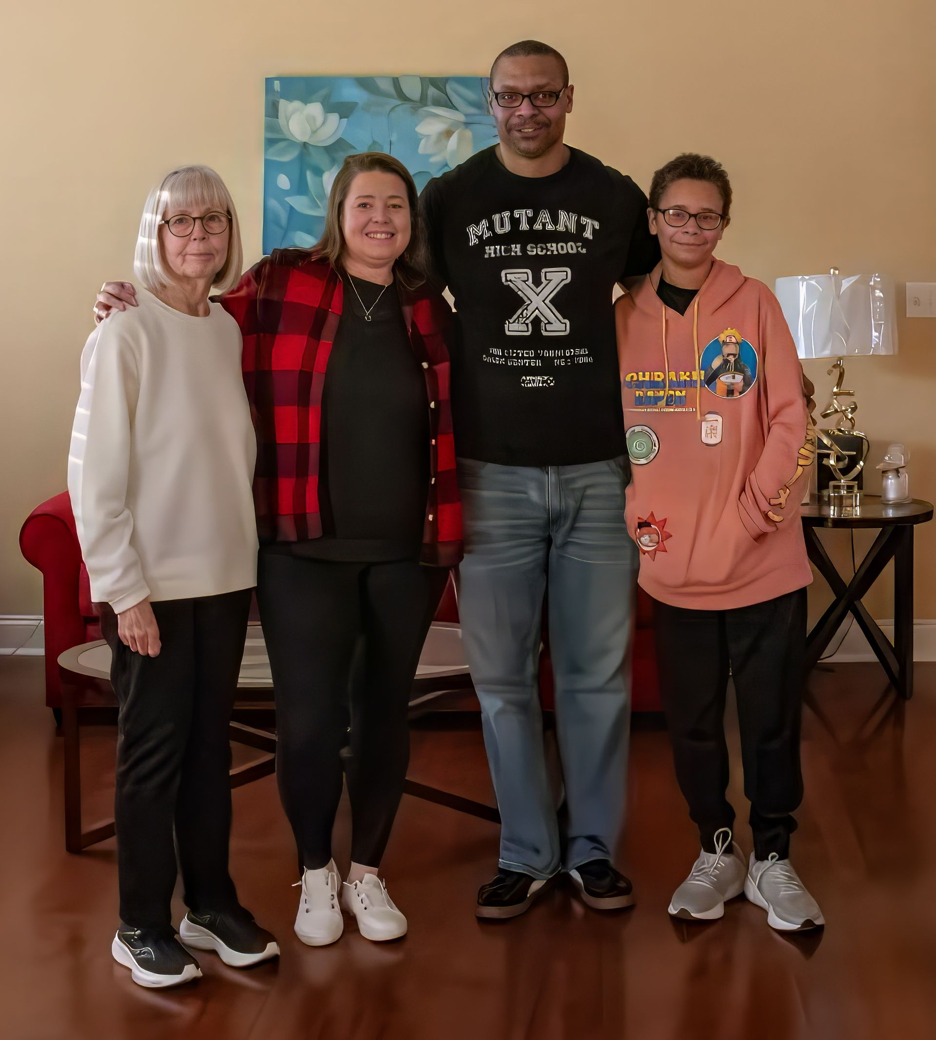 Four people stand smiling together in a living room, positioned in front of a blue floral wall hanging.