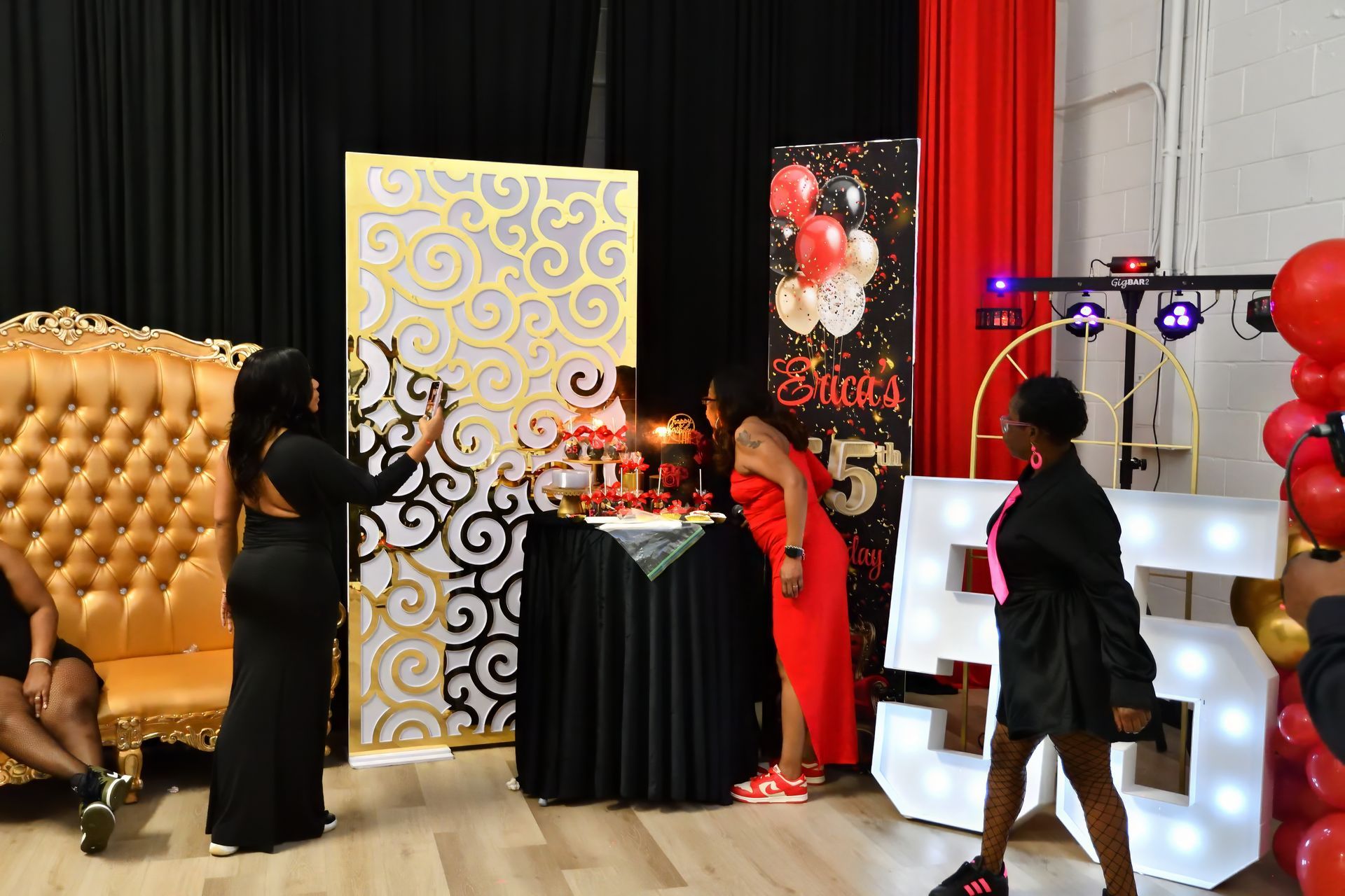 People gather at a party featuring a golden throne, a decorated table, and a large lighted number 55 display.