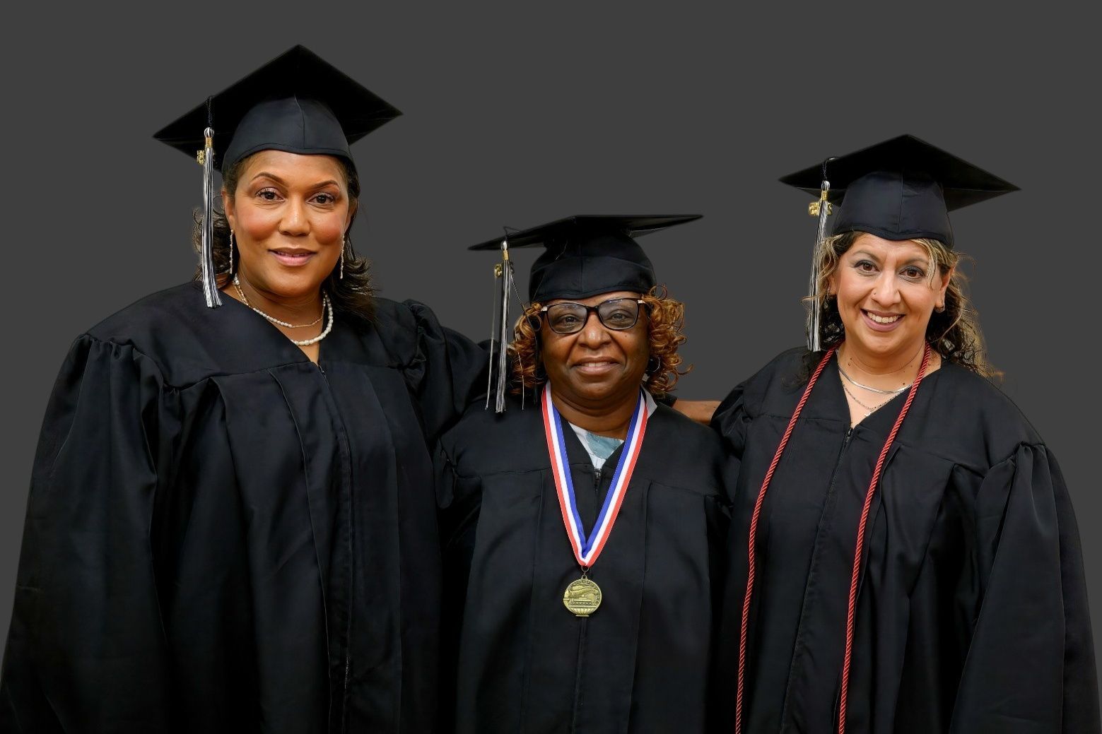 Three people wearing black graduation caps and gowns pose for a photo against a grey background.