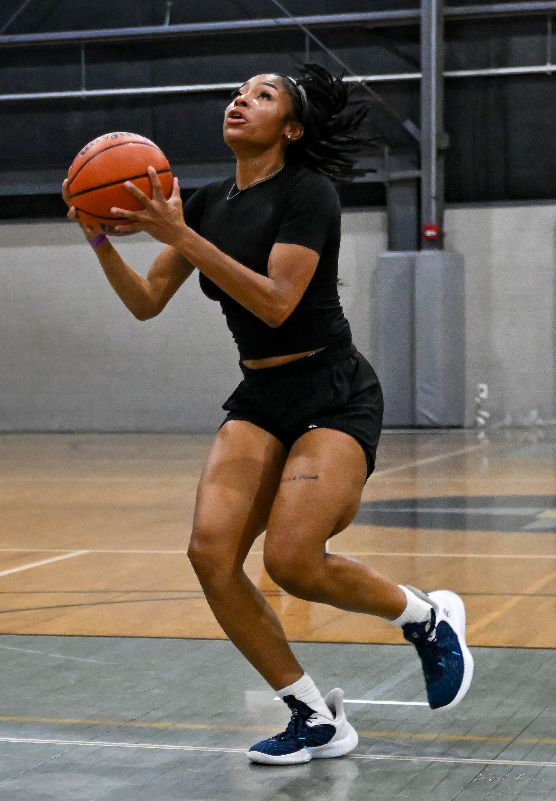 An athlete in black workout gear holds a basketball, preparing to shoot on an indoor court.