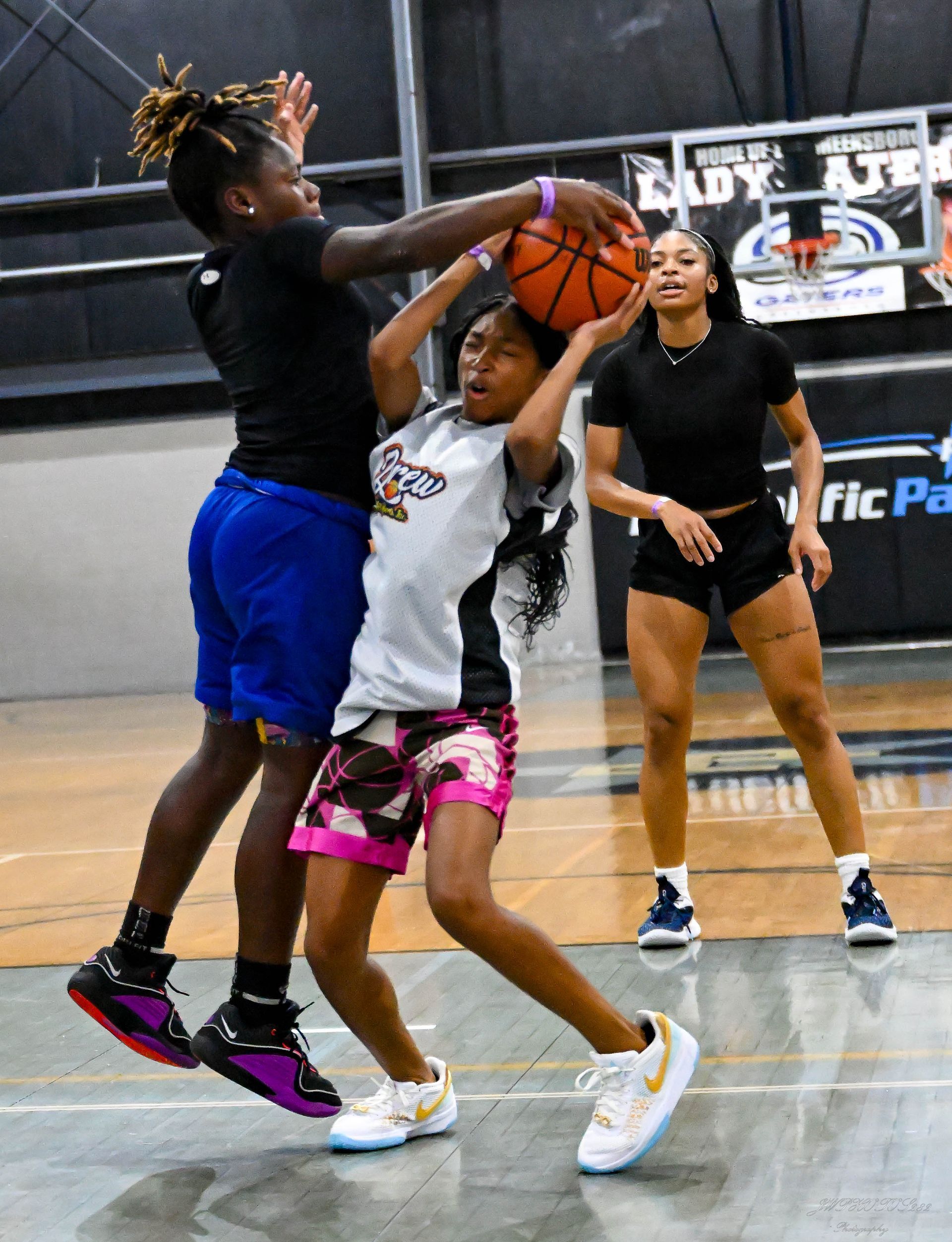 Two basketball players battle for a rebound as another player observes in a gym.