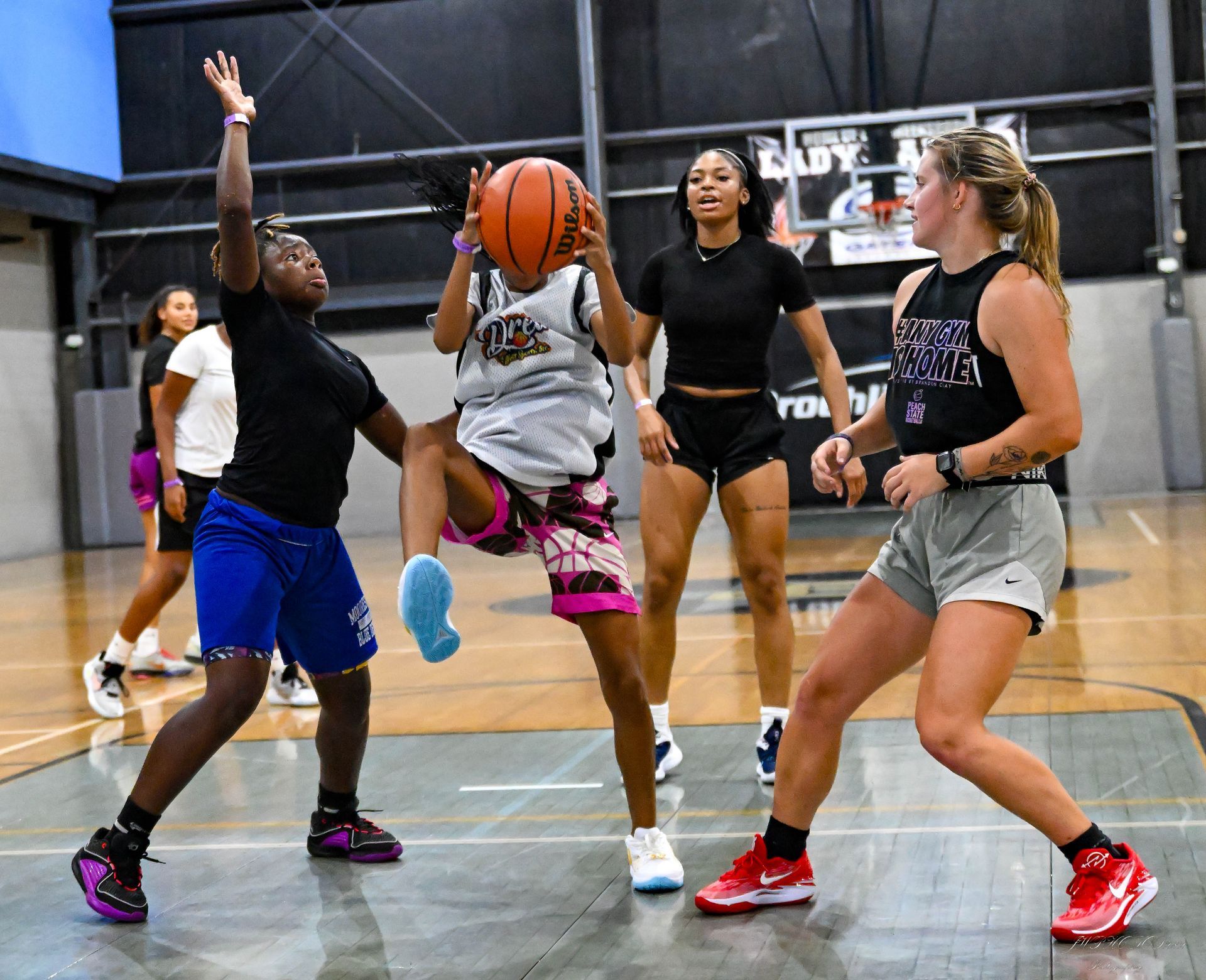 Basketball players in an indoor gym practice drills, with one player holding a basketball while being defended.