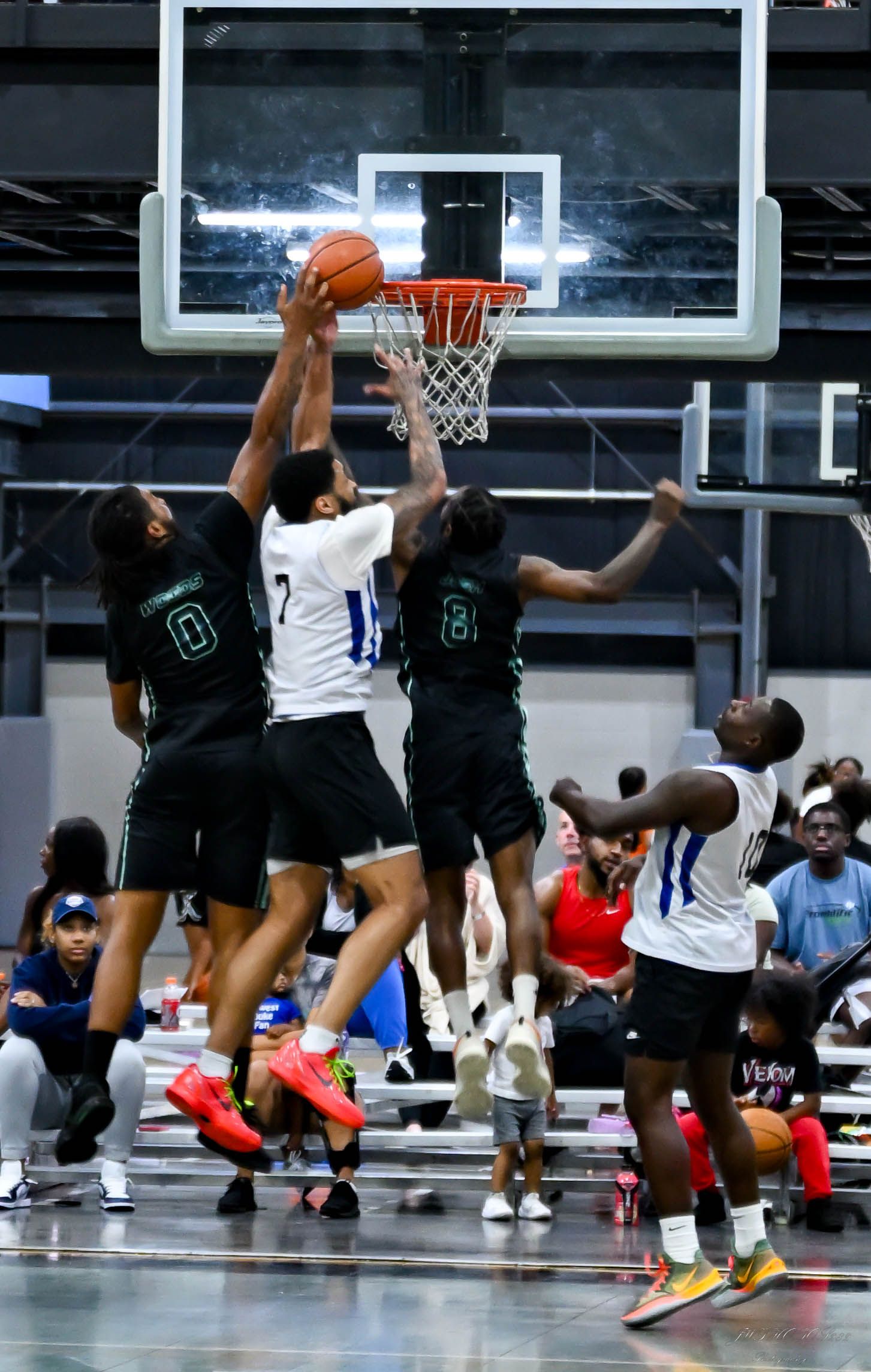 Basketball players in black and white jerseys compete for a rebound near the hoop during an indoor game.