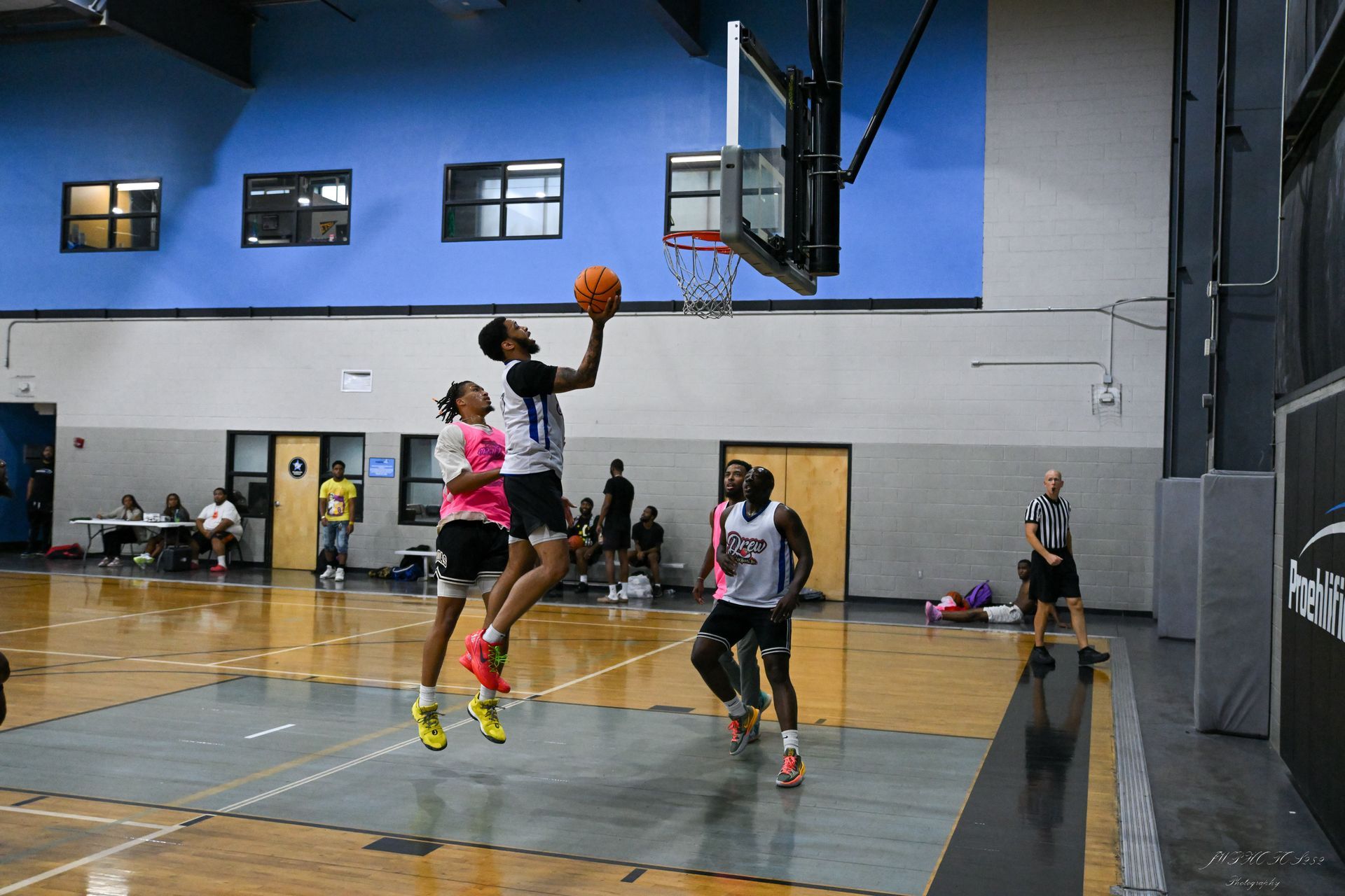 Players in jerseys compete during a basketball game on an indoor court, with one athlete reaching up to shoot the ball.