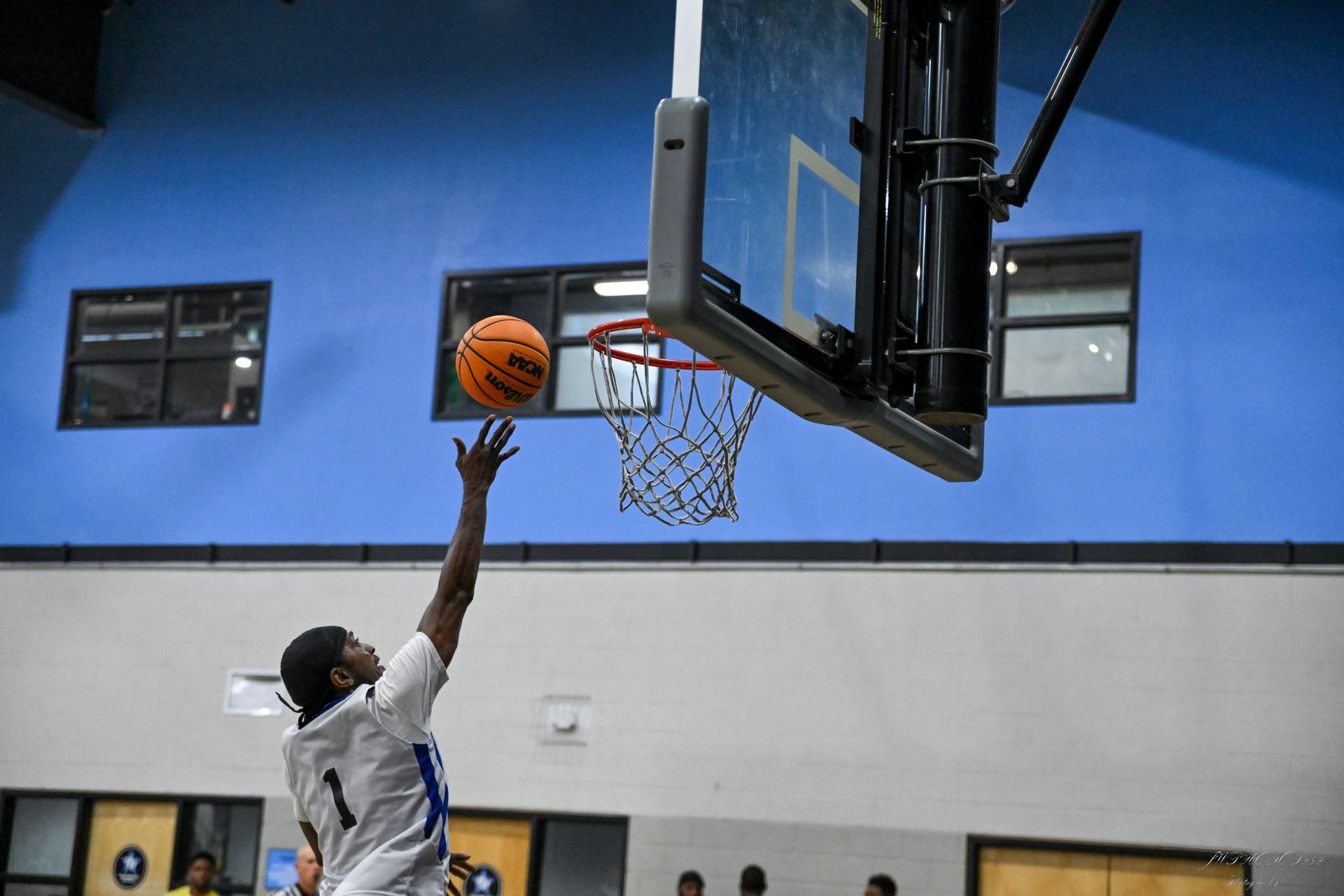 A basketball player in a white uniform reaches up to shoot a basketball toward a hoop in an indoor gym.