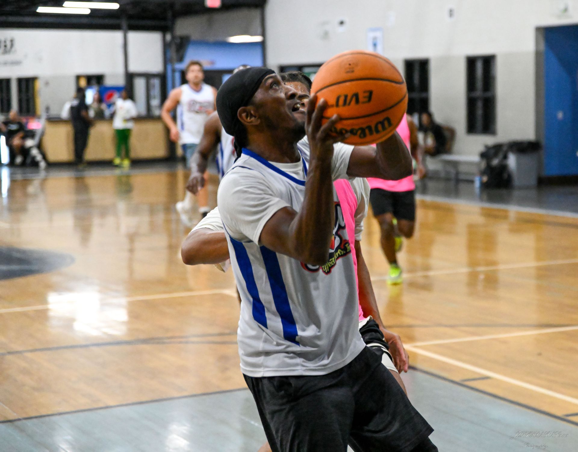 A basketball player in a white and blue jersey holds a basketball up to shoot during a game in an indoor gym.