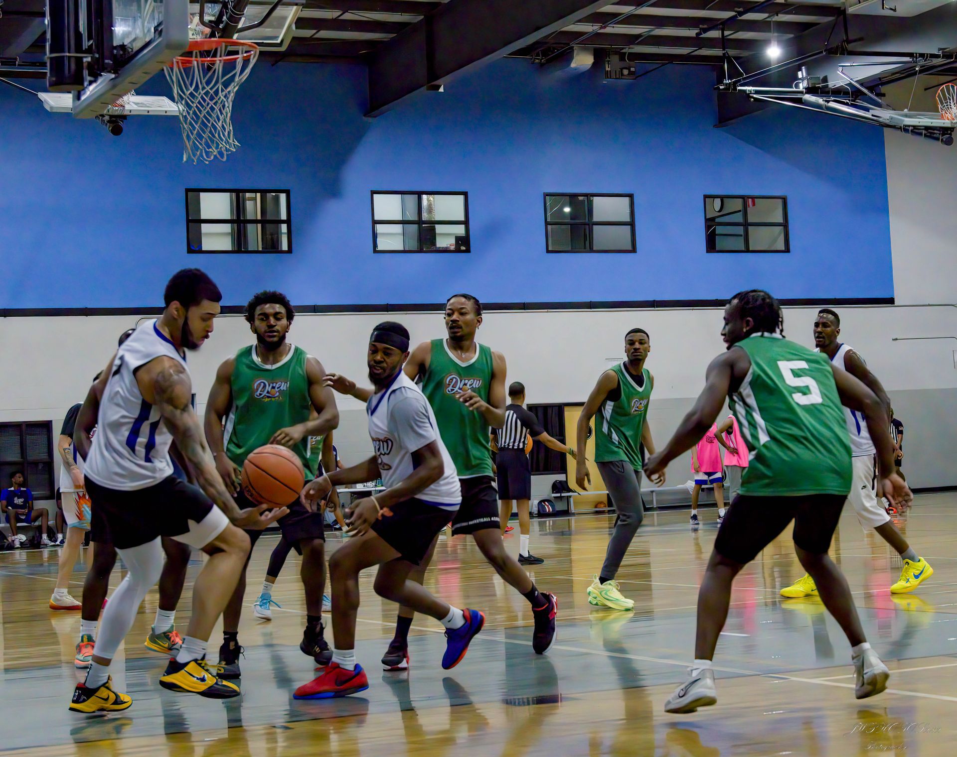 Athletes in green and white jerseys playing a basketball game on an indoor court.