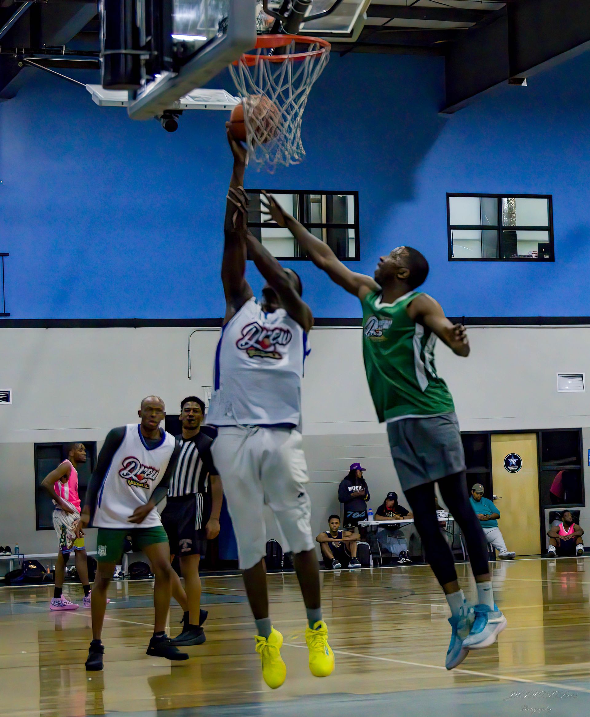 Two basketball players jump toward a hoop to contest a shot during an indoor game.