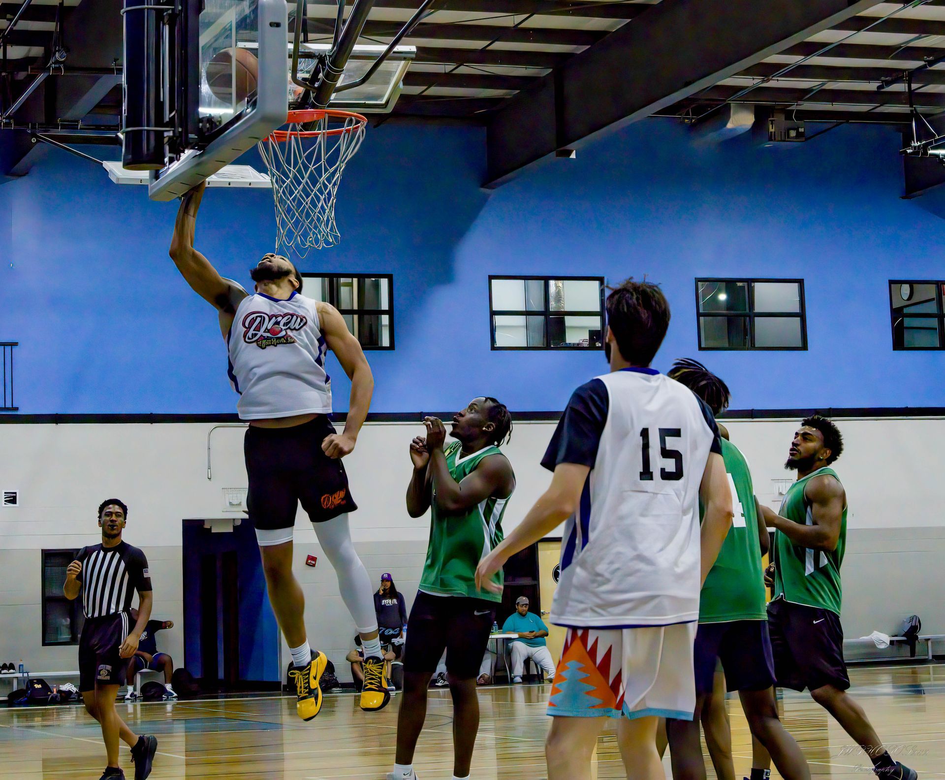 A basketball player reaches up for a layup during an indoor game while teammates and opponents watch from the court.