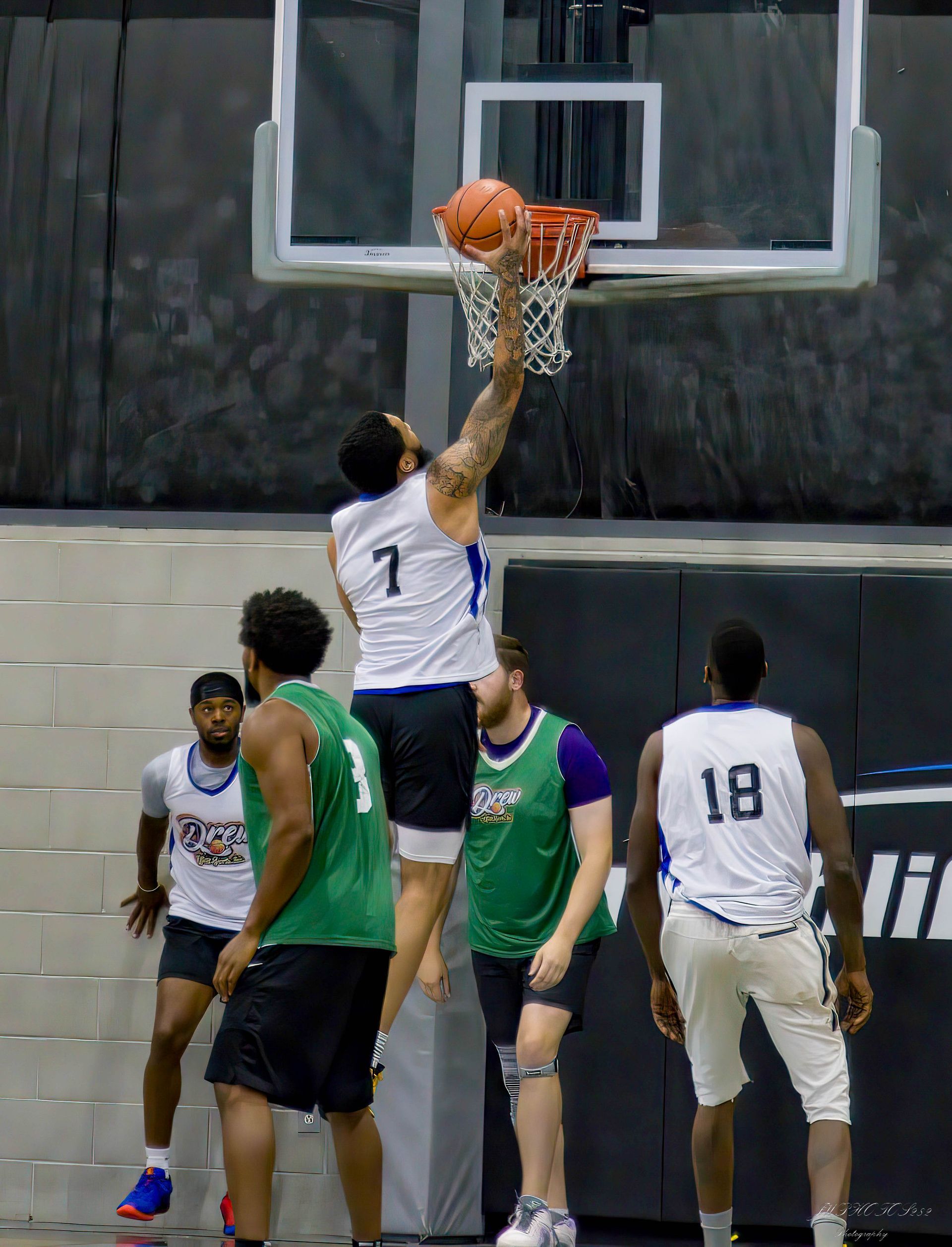 A basketball player in a white jersey with the number 7 dunks a basketball into the hoop while other players watch.