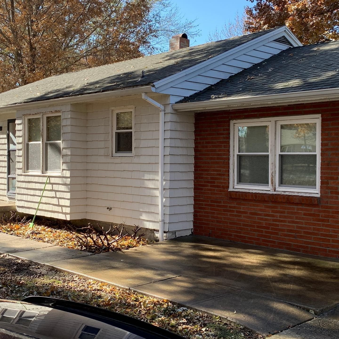 A single-story house with white horizontal siding and a red brick exterior section, featuring a driveway and a chimney.