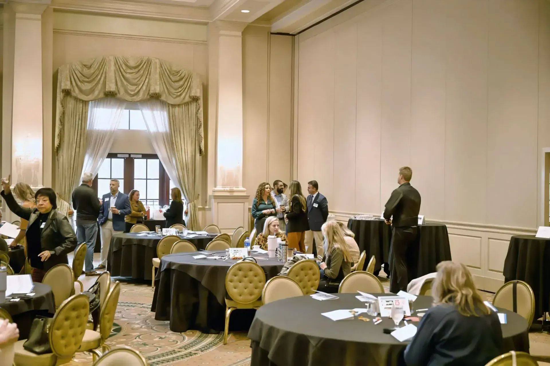 People network in an elegant ballroom featuring round tables with black tablecloths and ornate gold chairs.
