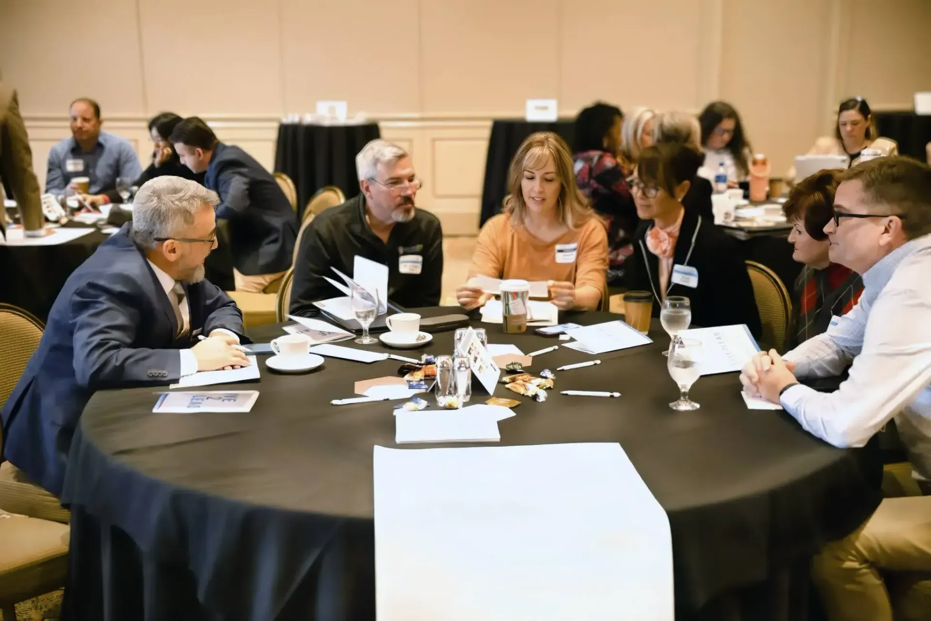 A group of people sit around a round table in a conference room, collaborating on documents during a meeting.