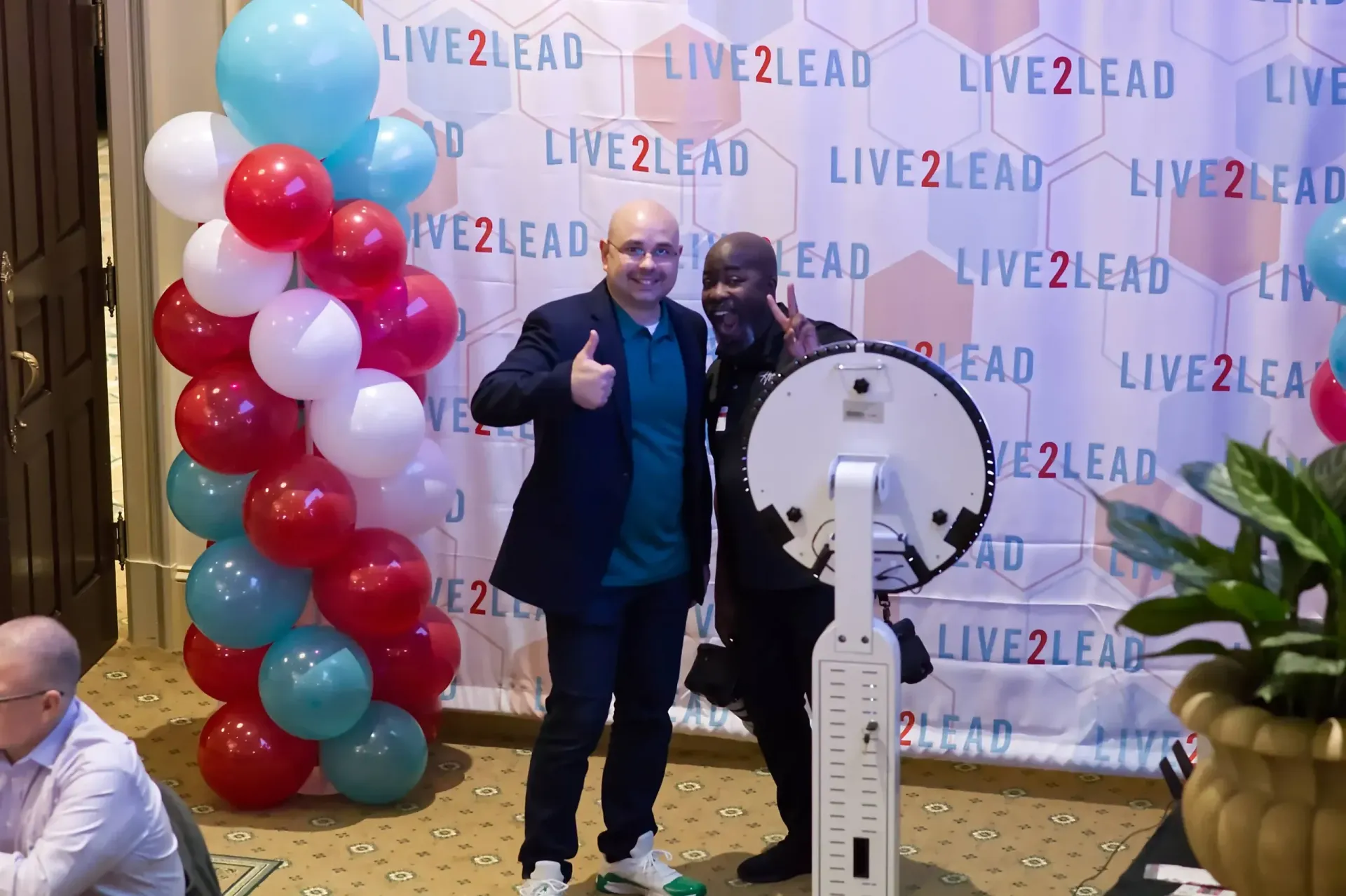 Two men smile and pose for a photo in front of a branded