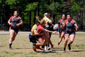 Rugby players in team uniforms run across a field, with one player passing the ball during a competitive match.