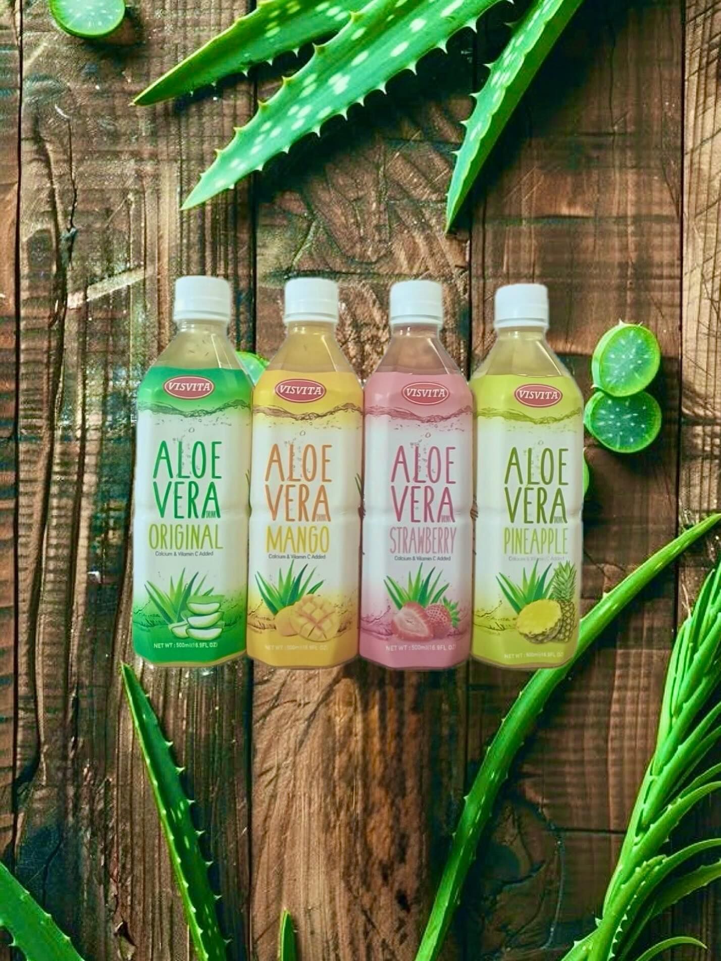 Four bottles of aloe vera juice in various flavors, surrounded by aloe vera leaves and wood background.