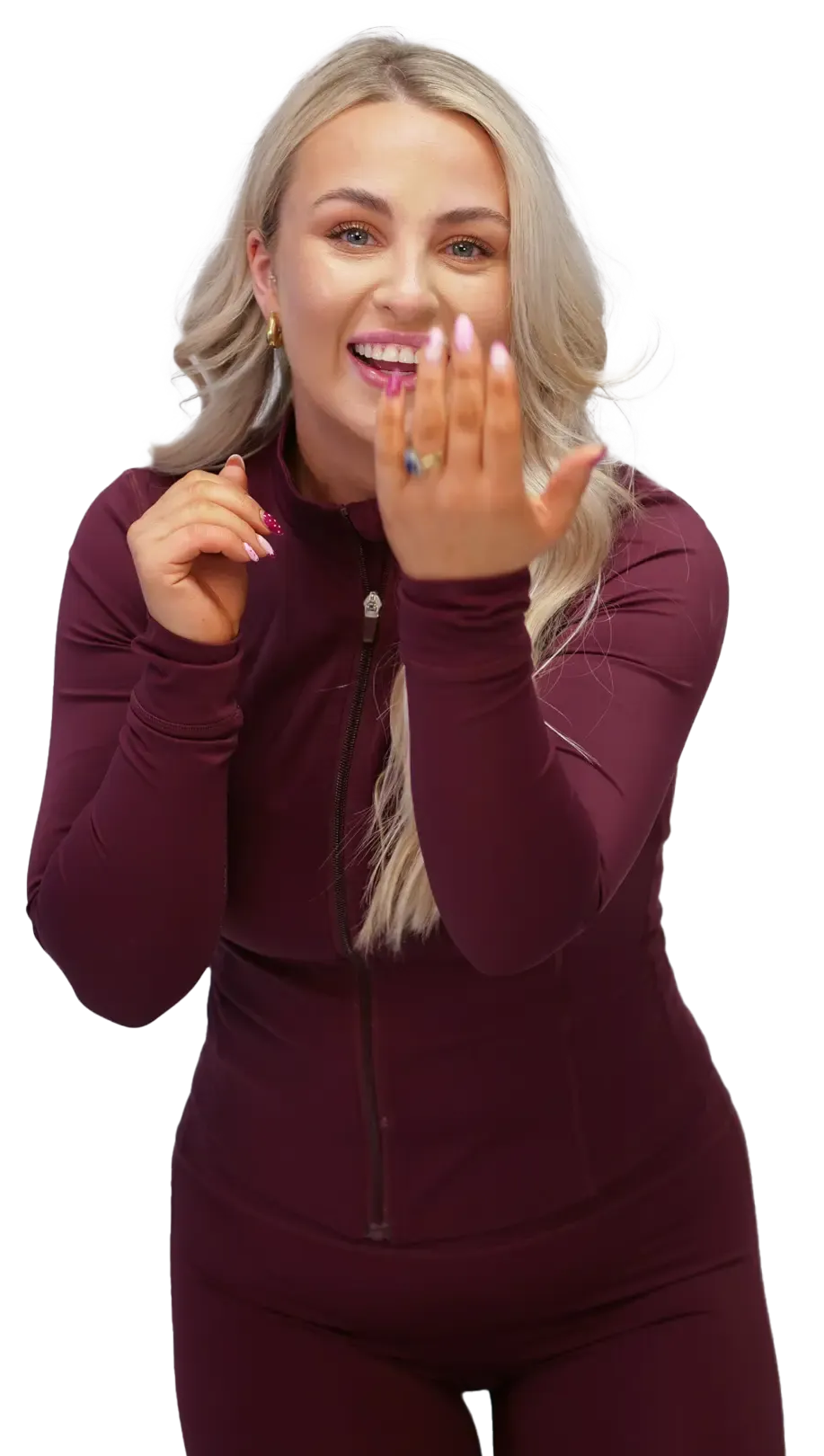 Woman in maroon athletic wear smiling, holding up hand with ring.