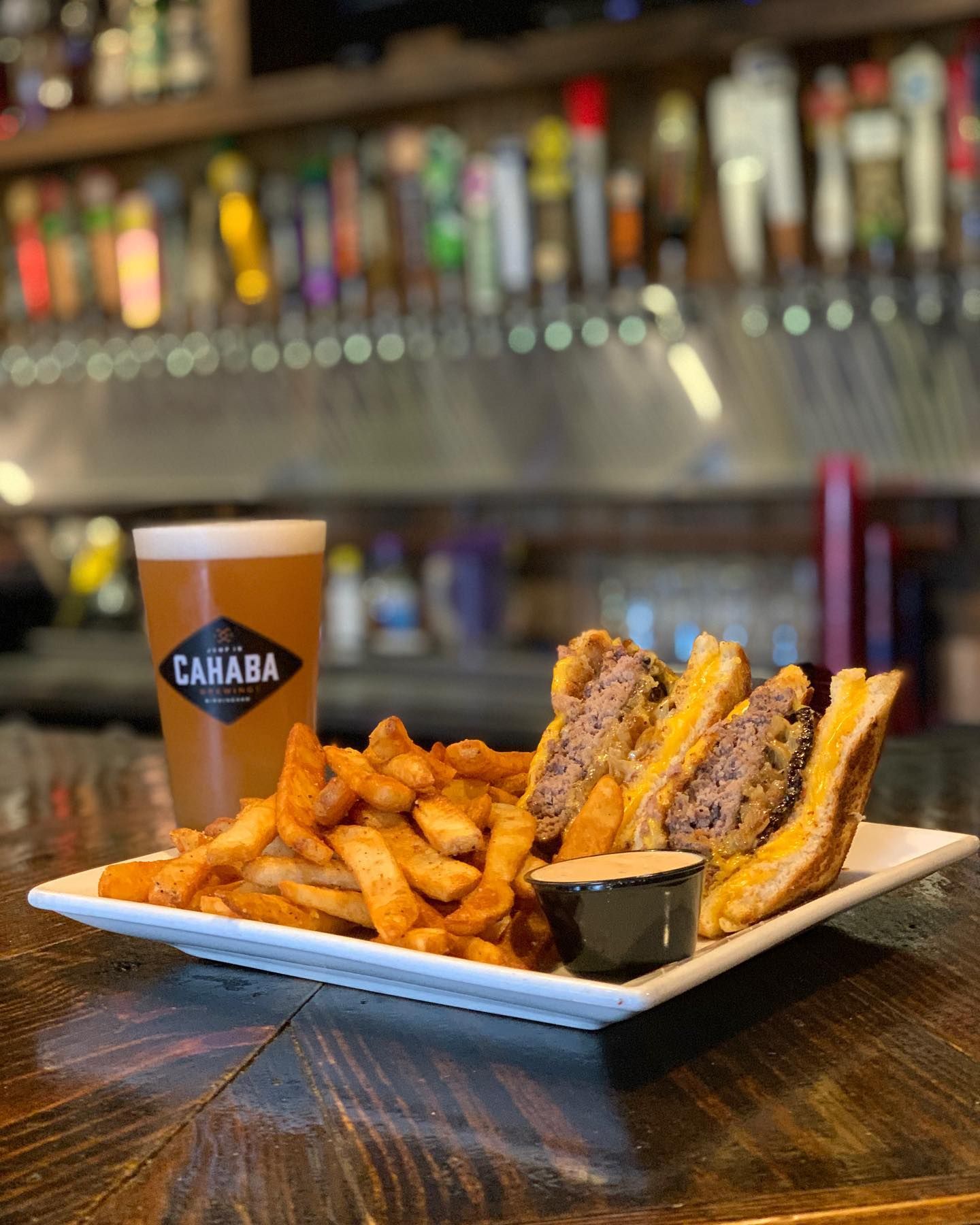 A person is holding a hamburger in front of a plate of french fries.