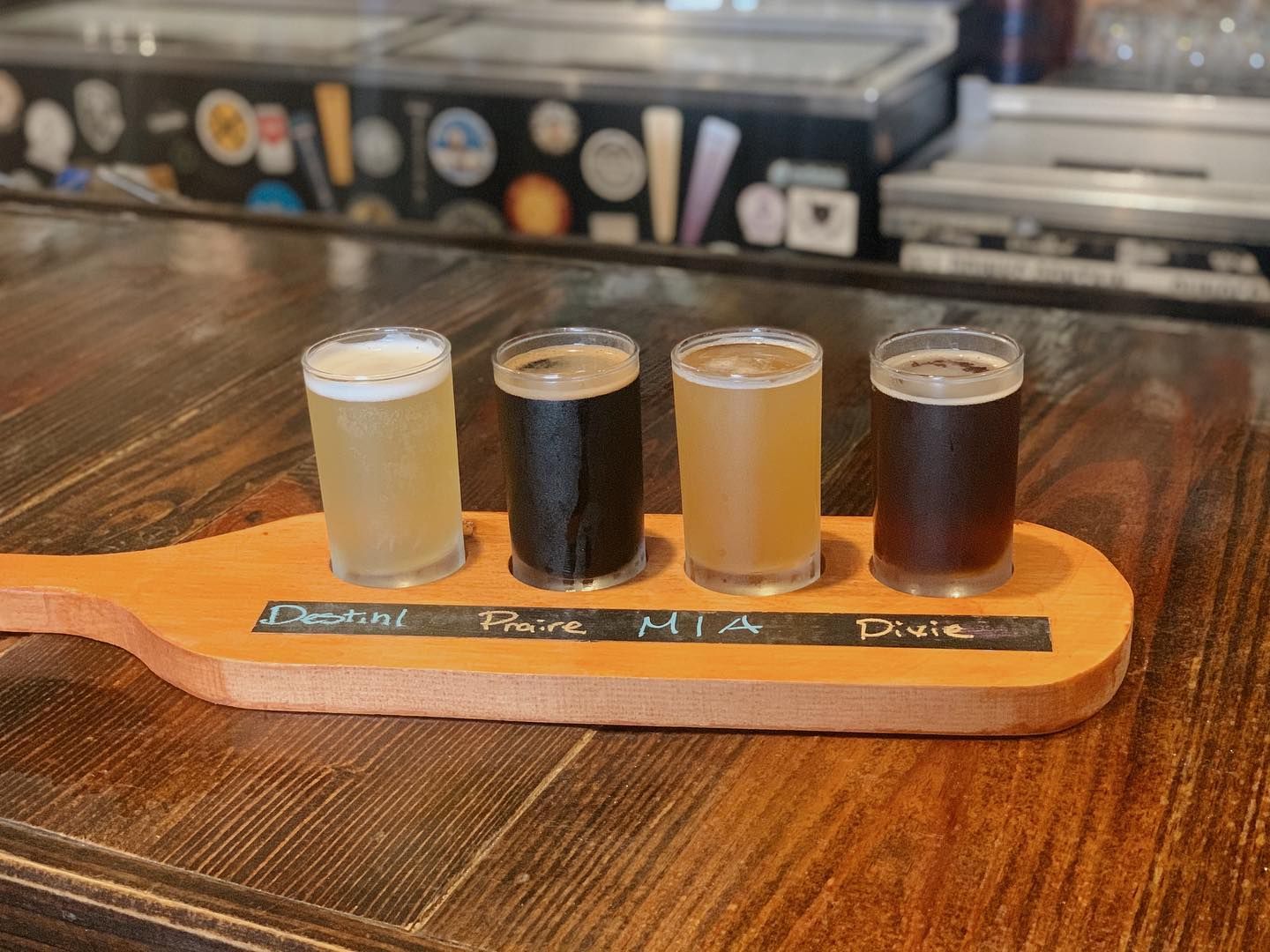 Four glasses of beer are on a wooden paddle on a wooden table.