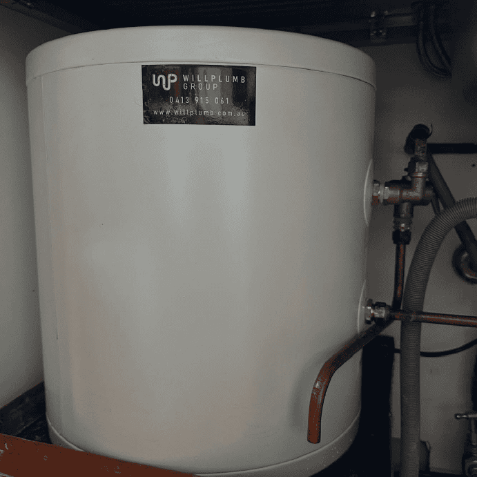 A white cylinder-shaped water heater with plumbing connections on its right side, situated in a storage space.