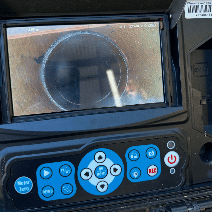 A portable drain inspection camera with a screen displaying a view inside a dark, cylindrical pipe.
