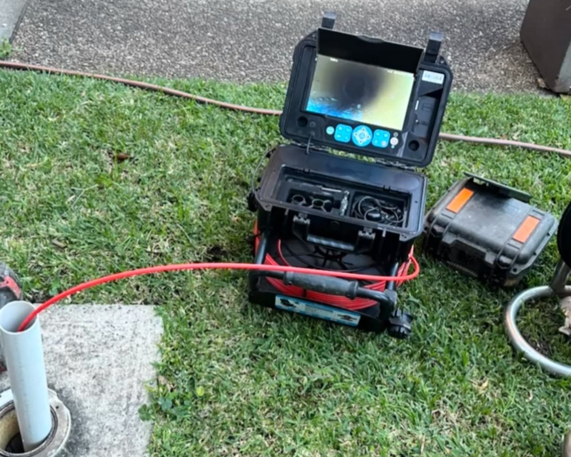 A sewer inspection camera system with a monitor display, set up on grass next to an open pipe access point.