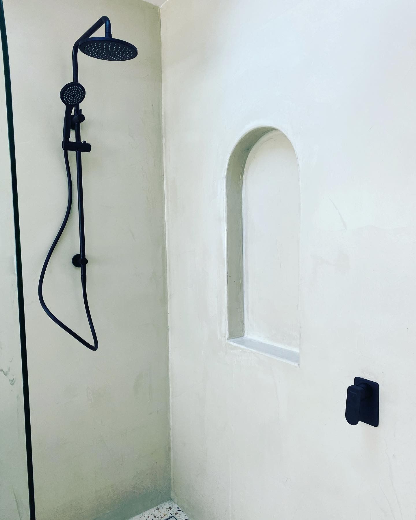 A matte black shower head and handle set against a light-colored wall with an arched recessed storage niche.