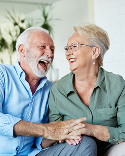 Two people laughing together, holding hands while sitting in a brightly lit indoor space.