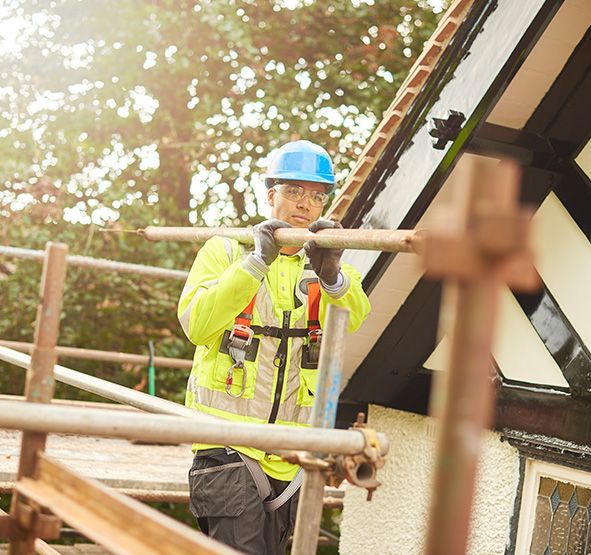 a man wearing a hard hat and safety vest is standing on a scaffolding.