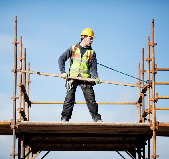 A construction worker is standing on top of a scaffolding holding a pole