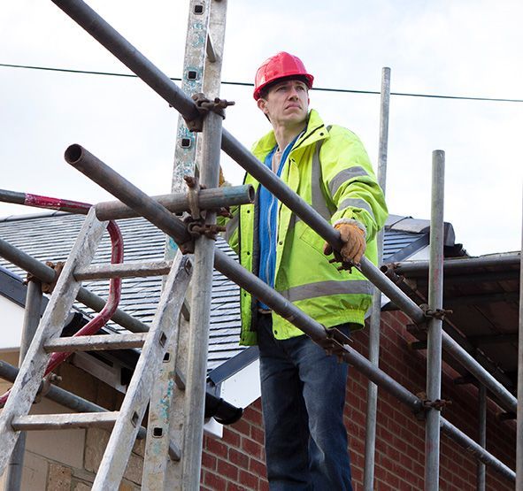 A man wearing a red hard hat is standing on a scaffolding