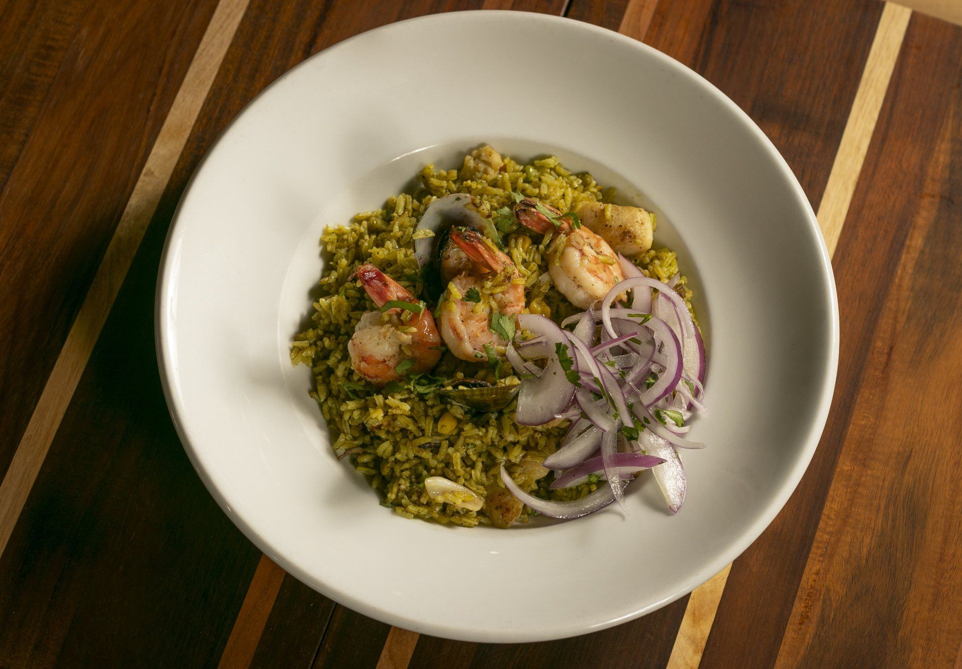 Shrimp and rice dish with red onion garnish on a white plate, wooden table.