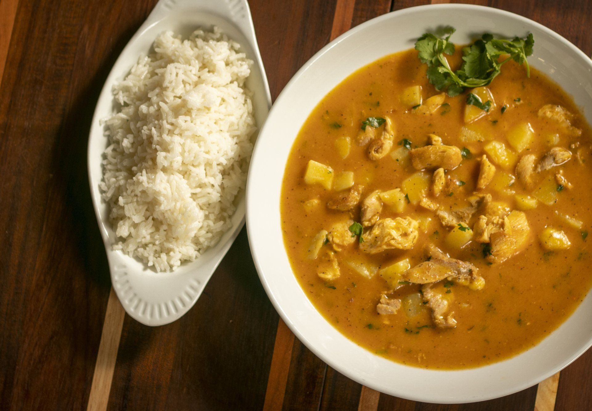 Chicken stew with potatoes, served with white rice on a wooden table.