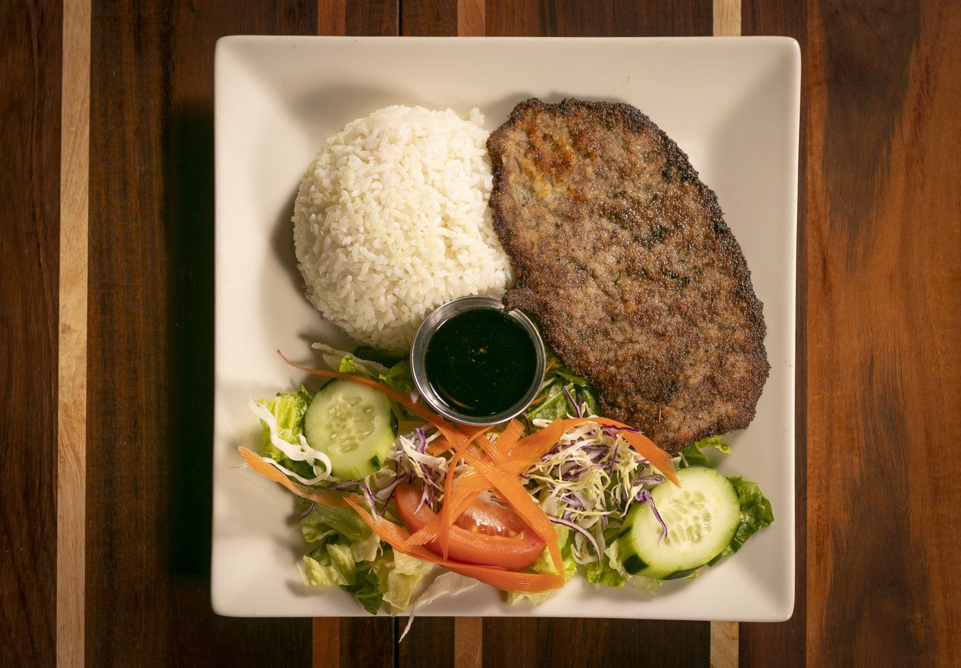 Plate with meat, rice, salad, and dipping sauce on a wooden table.