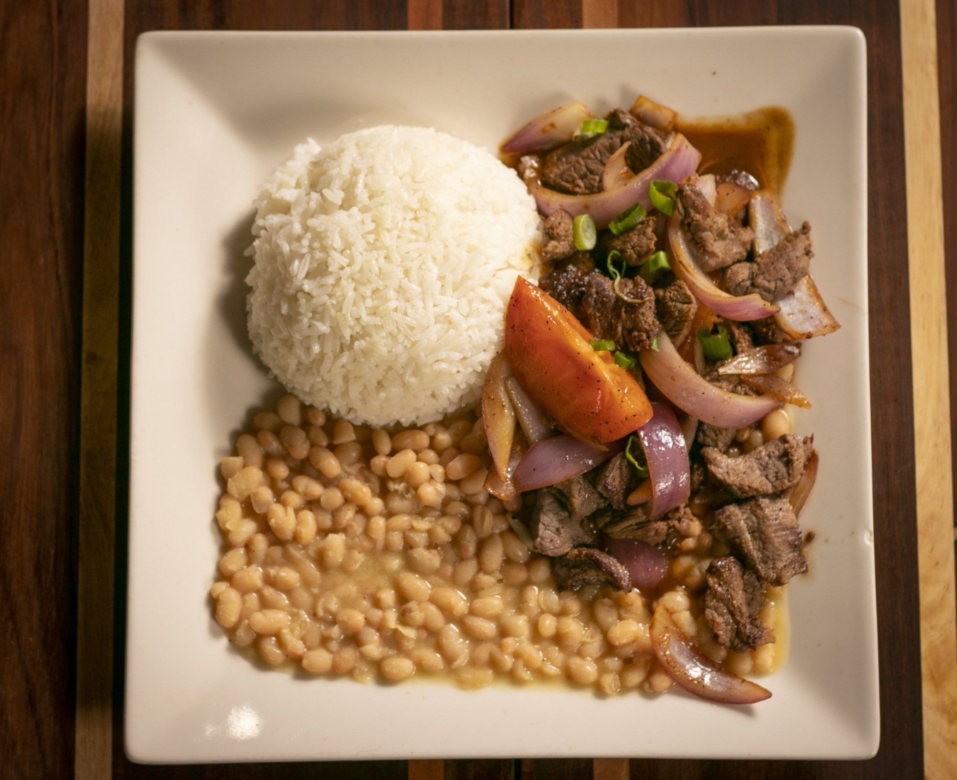 Lomo saltado with rice and beans, a Peruvian dish on a white plate.