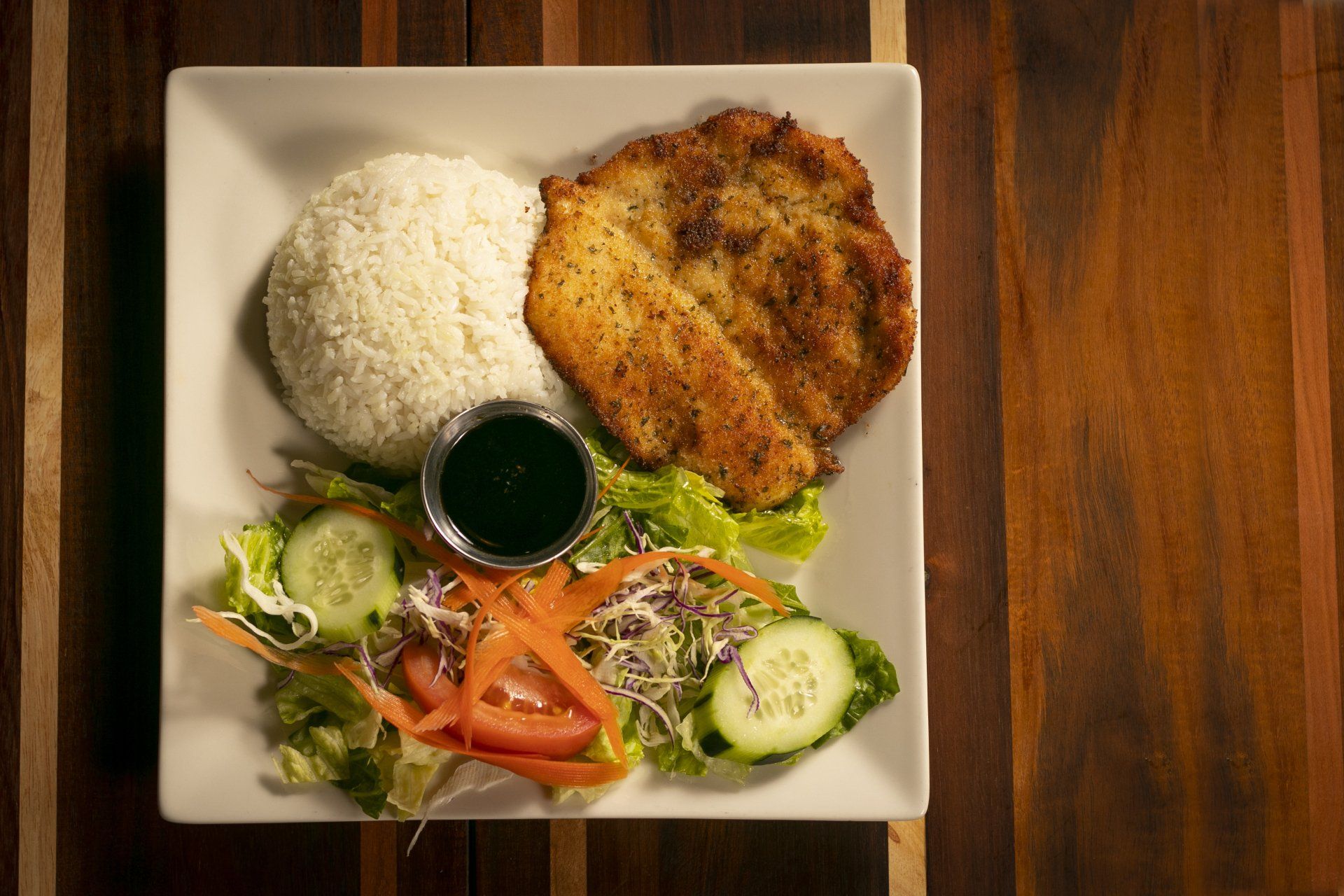 Plate of food: chicken cutlet, rice, salad with a small cup of green sauce.