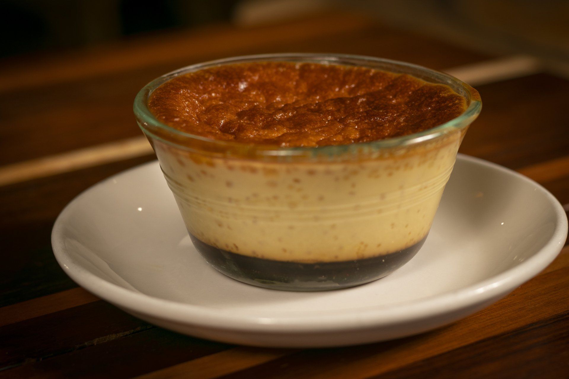 A creamy custard dessert in a glass ramekin, set on a white saucer. The top is a caramelized golden brown.