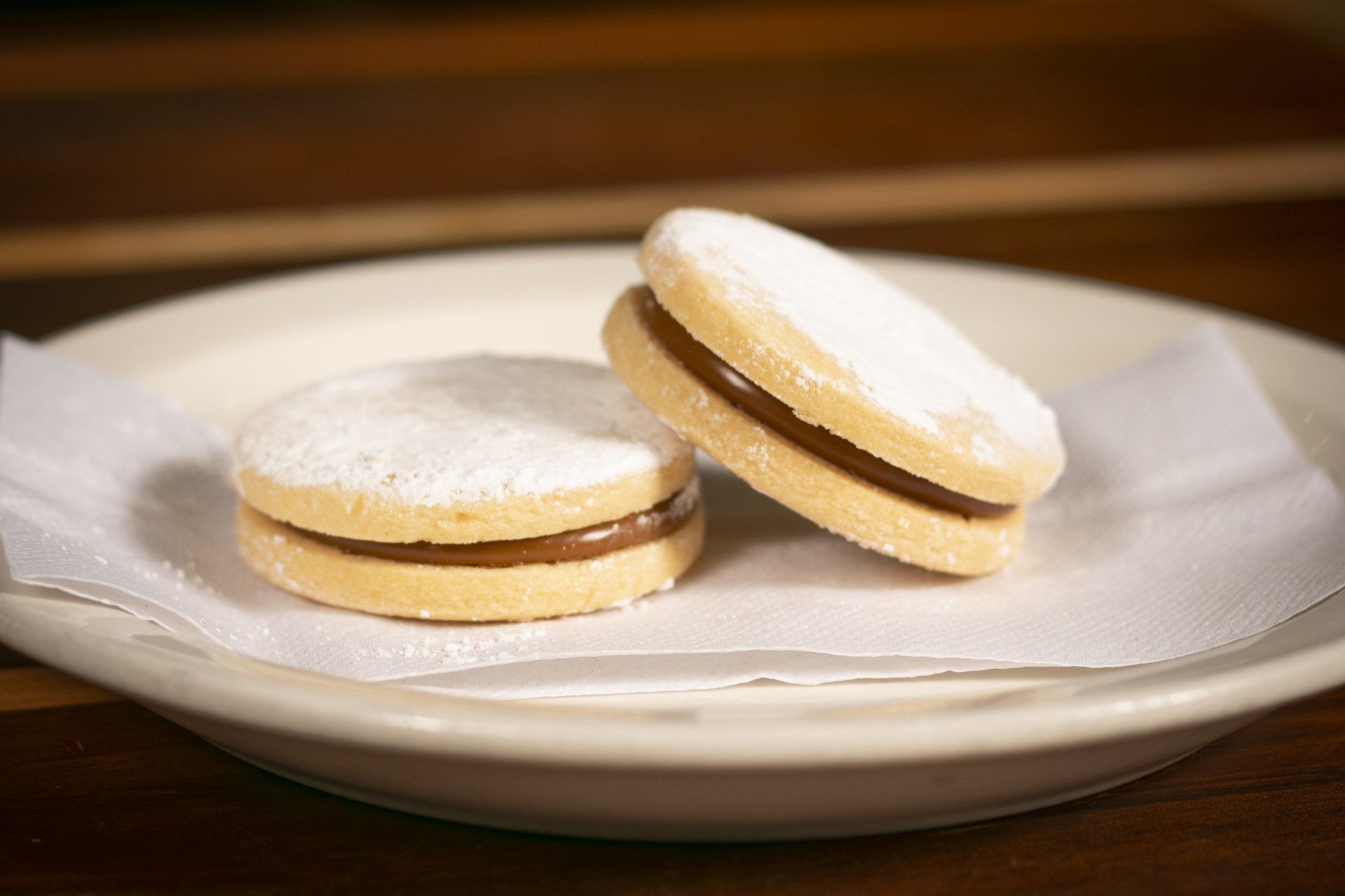 Two round cookies filled with caramel, dusted with powdered sugar, on a white plate.