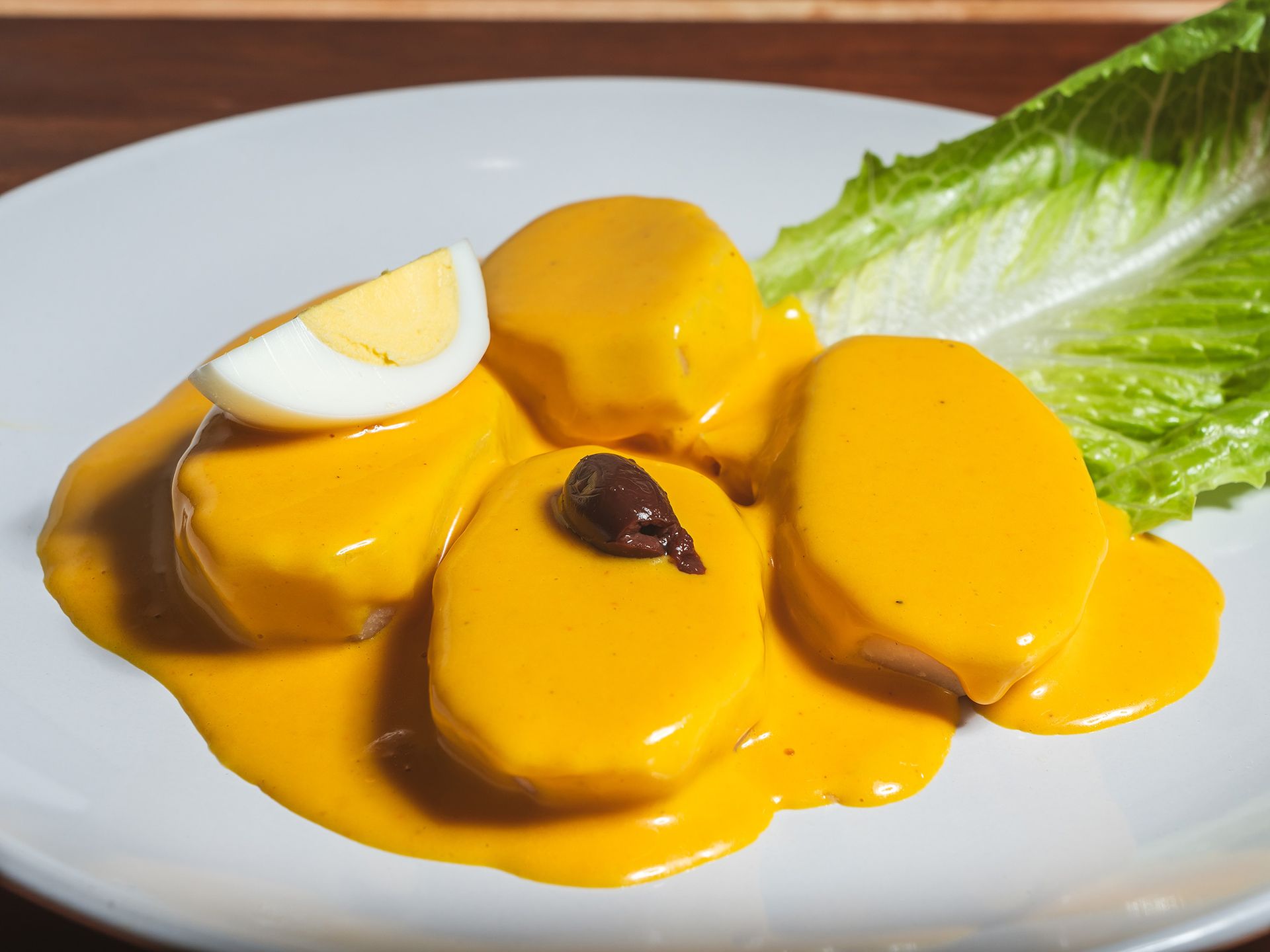 Peruvian causa with yellow sauce, egg, and olive on a white plate, with lettuce.