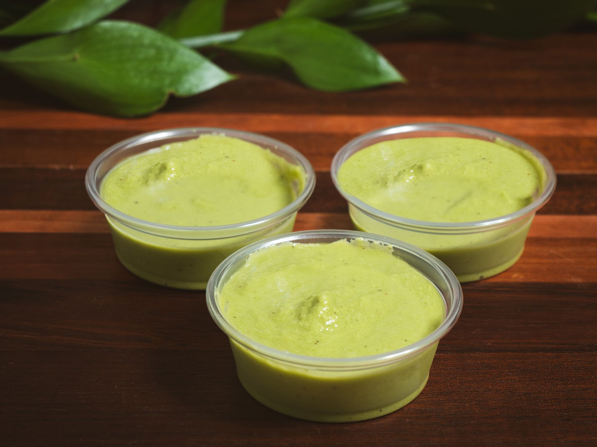 Three small containers of green dip on a wooden surface, with leafy green garnish.