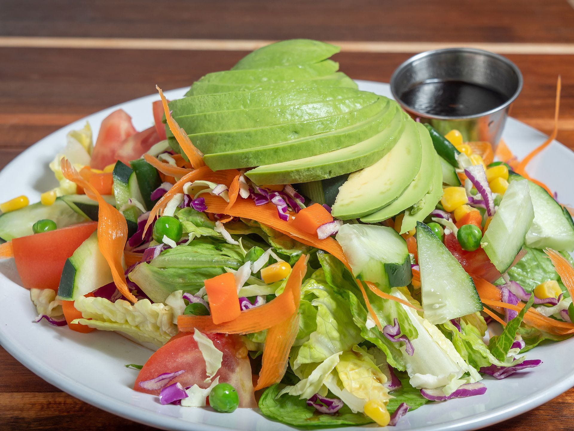 Salad with avocado slices, mixed vegetables, and dressing on a white plate.