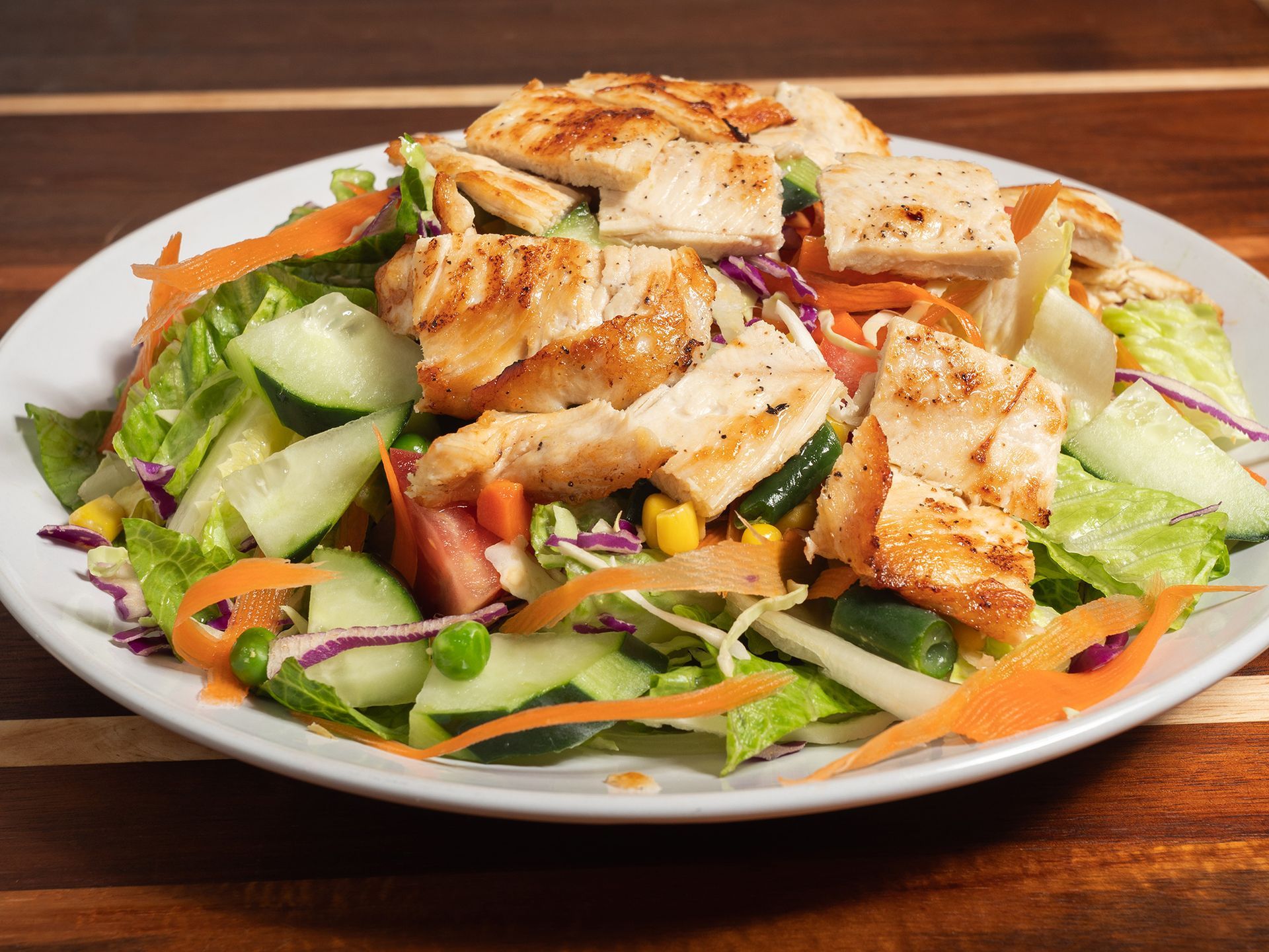 Chicken salad with grilled chicken, vegetables, and dressing on a white plate.