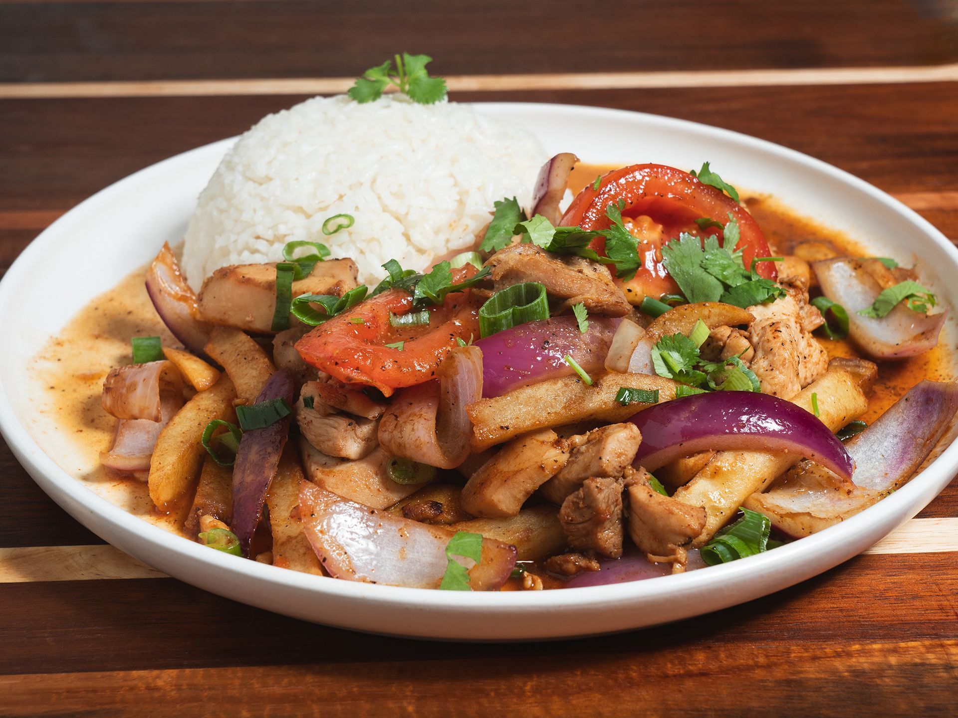 A plate of Peruvian Lomo Saltado with rice, beef, onions, tomatoes, and cilantro.