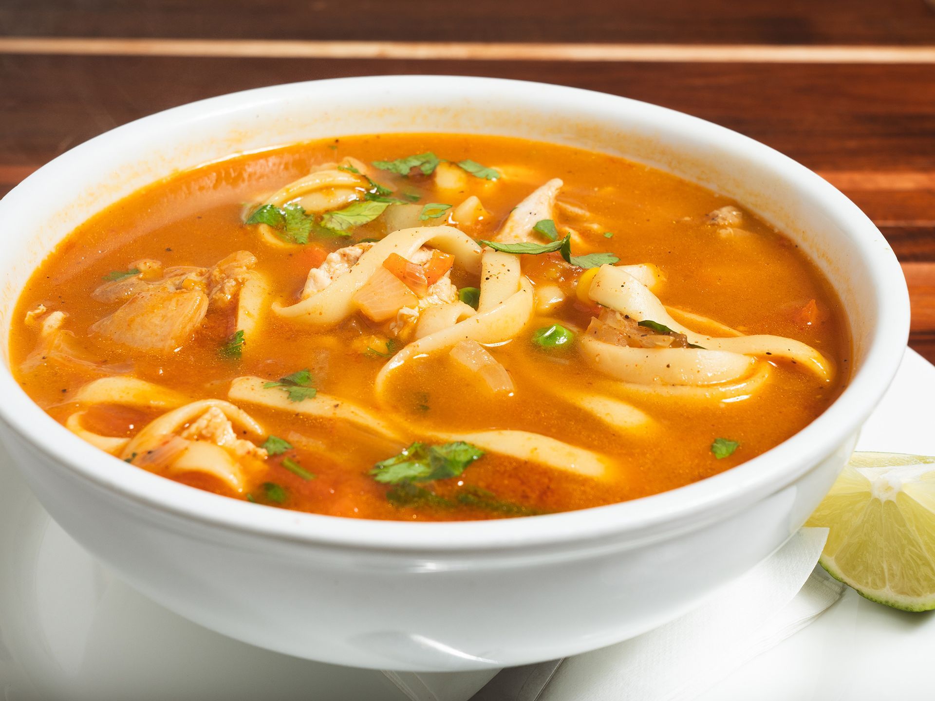 Bowl of orange seafood soup with noodles, garnished with cilantro and lime.