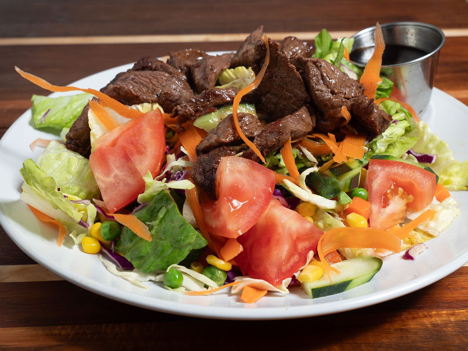 Steak salad with tomatoes, carrots, and dressing on a white plate.