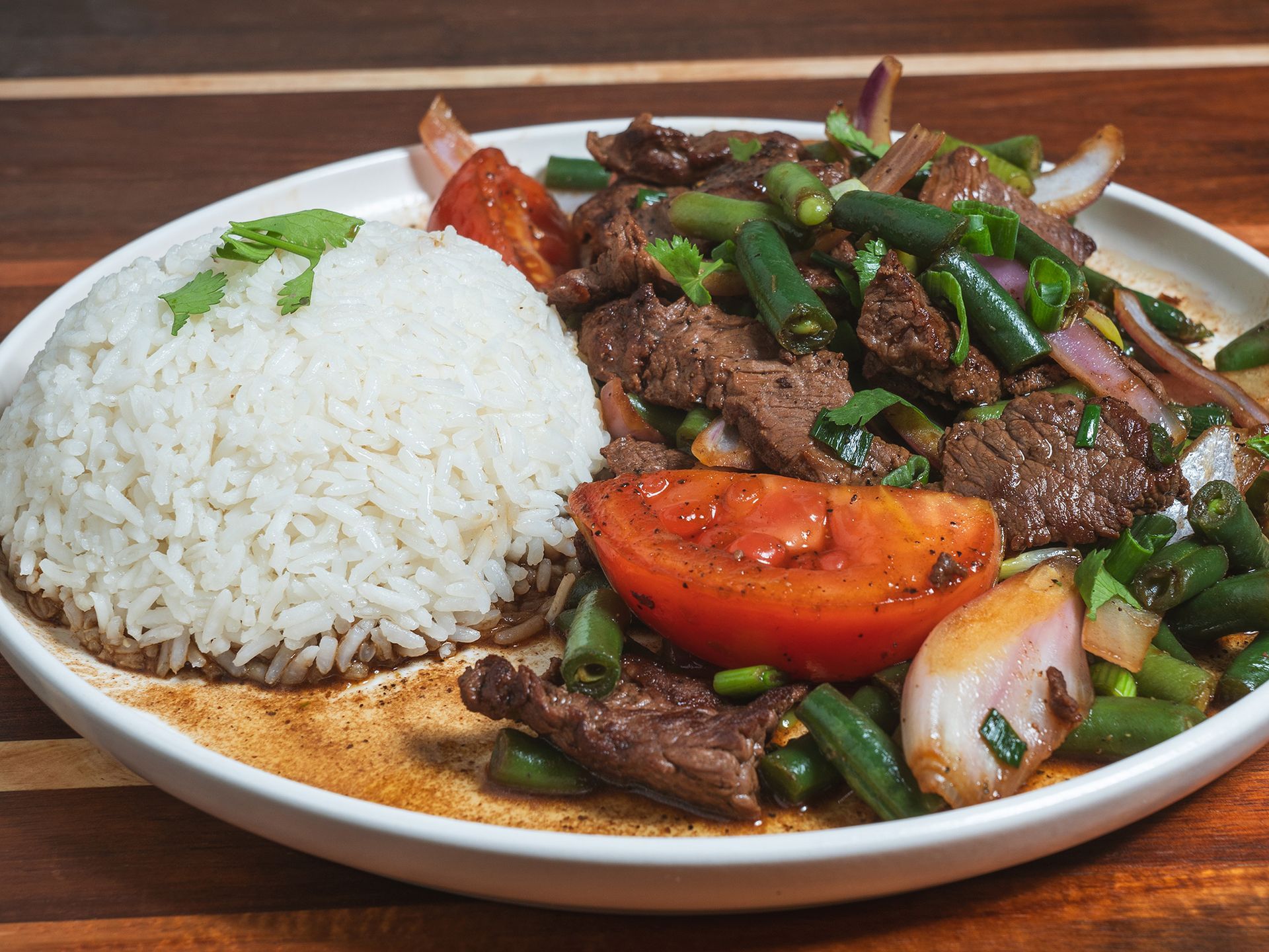 Plate of Peruvian Lomo Saltado with rice, beef, tomatoes, onions, and green beans.
