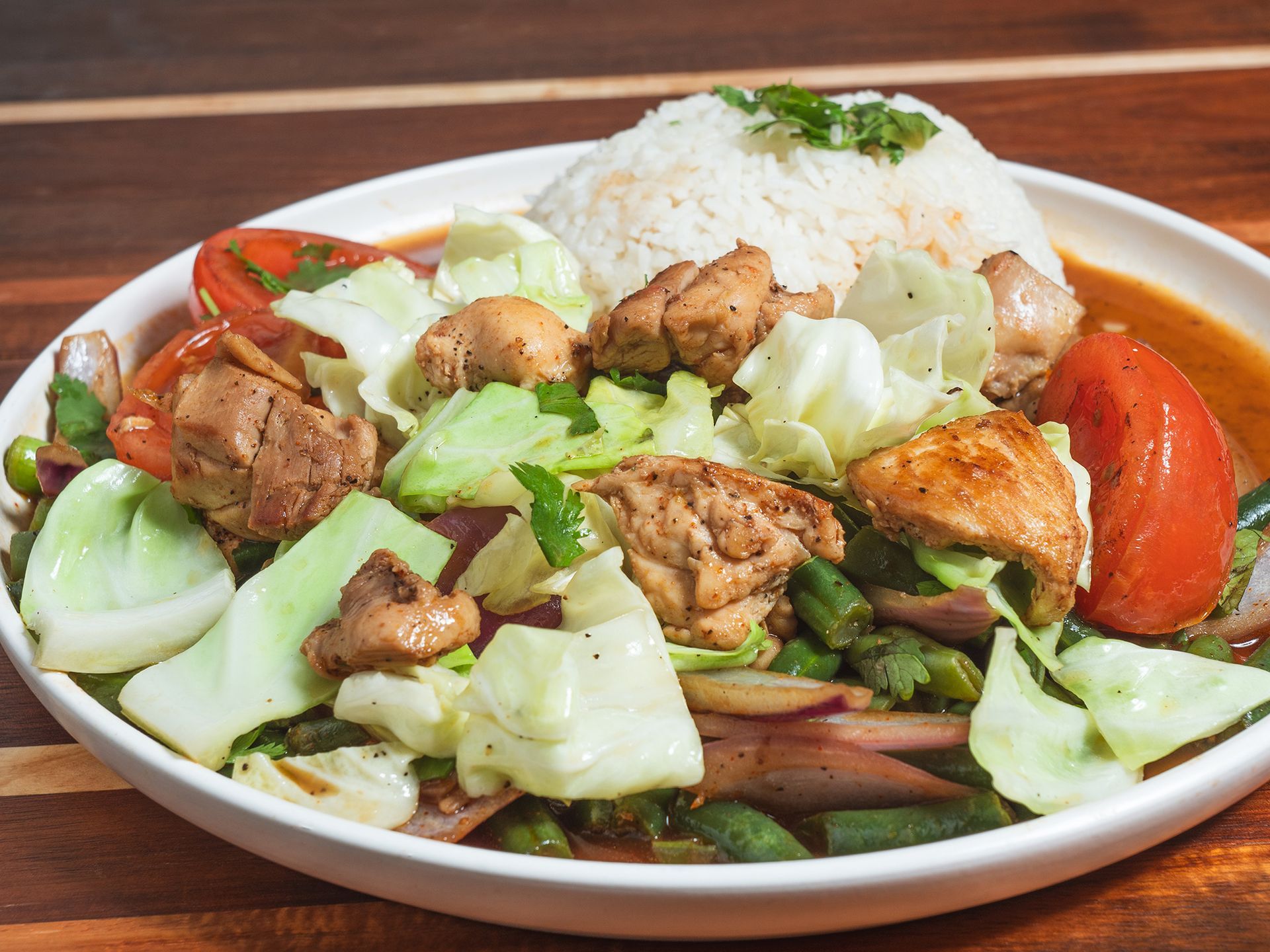 Chicken stir-fry with white rice, cabbage, tomatoes, and green beans on a white plate.