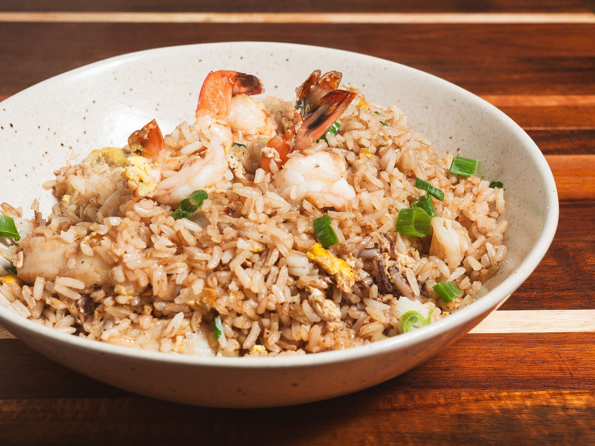 Shrimp fried rice in a white bowl on a wooden table, garnished with green onions.